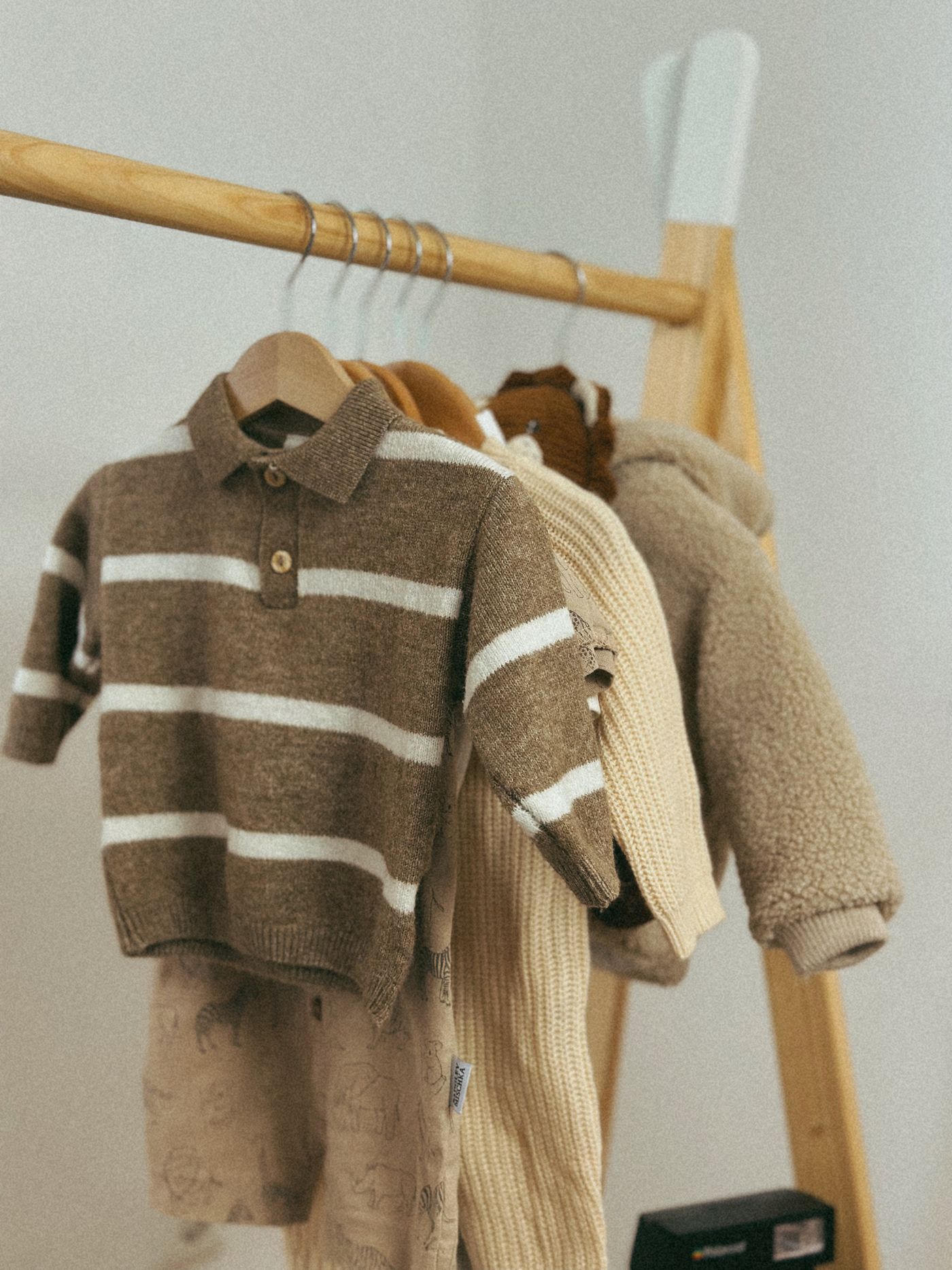Neutral-colored children’s knitwear hanging on a wooden clothing rail.